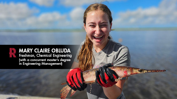 Mary Claire Obluda laughs as she clutches a fish in her gloved hands, with a body of water stretching behind her.
