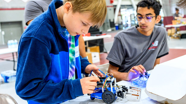 Two students work together to wire a robot.