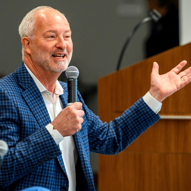 Steve Hill and President Robert A. Coons both sit in front of an audience in the Lake Room, each holding a microphone.