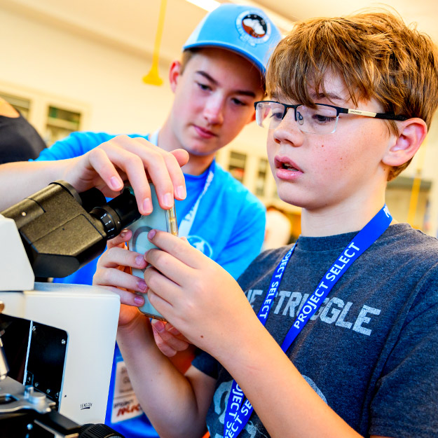 Two students wearing Project SELECT lanyards examine liquid in a beaker in a lab.
