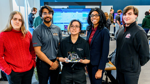 Five Rose-Hulman students pose with their senior design project during a presentation session.