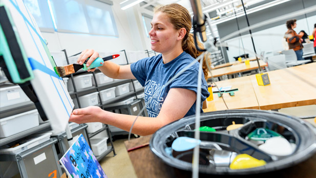 A student paints on an adjustable easel her team built. 
