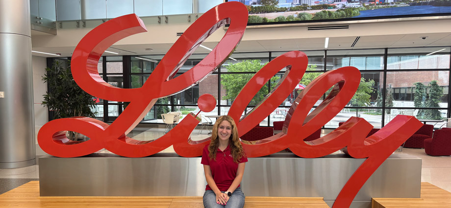 Claire Allen sits in front of the Eli Lilly and Company logo.