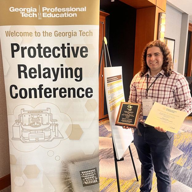 Mason Cooper holds an award plaque by the conference banner.