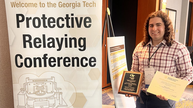 Mason Cooper holds an award plaque by the conference banner.