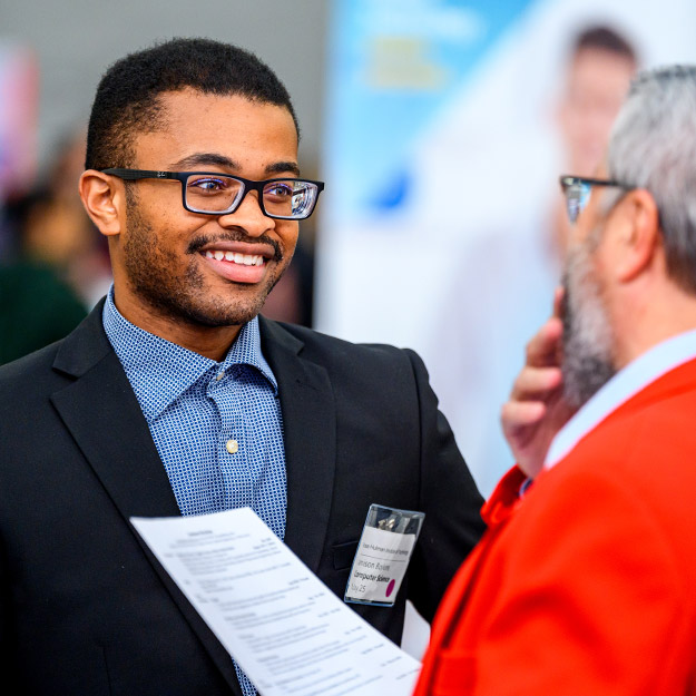 A smiling male student greets an employer at the Career Fair.