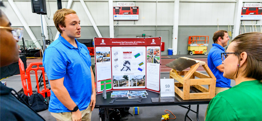 A student stands next to a prototype of the greenhouse roof on a table.