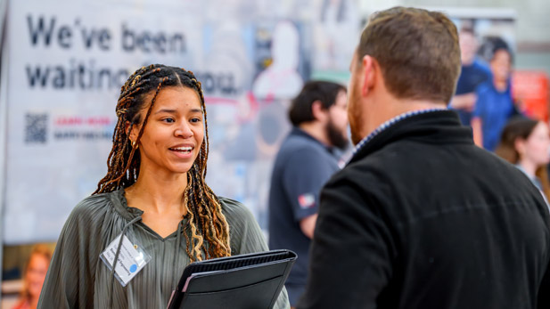 A smiling student holding a portfolio greets an employer at the Career Fair.