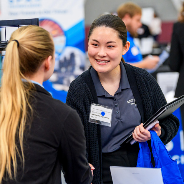 A smiling student holding a portfolio greets an employer at the Career Fair.